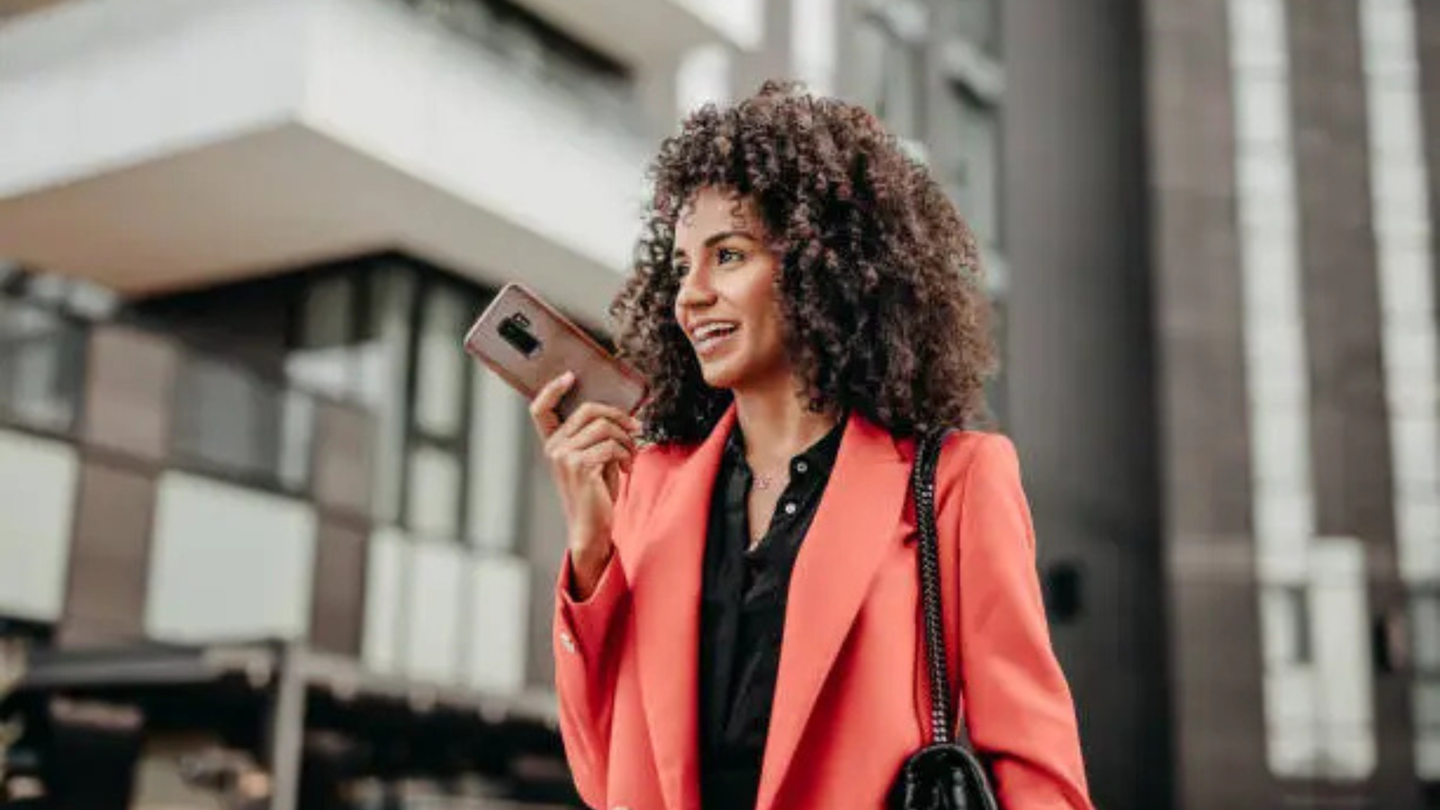 A smiling woman using her smartphone for a voice command, symbolizing the growing trend of voice search for local businesses.